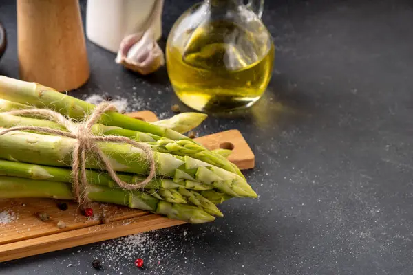 Çiğ organik kuşkonmaz mutfak masasının arka planında bir sürü ev yapımı yeşil kuşkonmaz pişirmeye ve kesme tahtasının üzerinde hazır. Yaz hasadı, yaz yemeği malzemeleri.