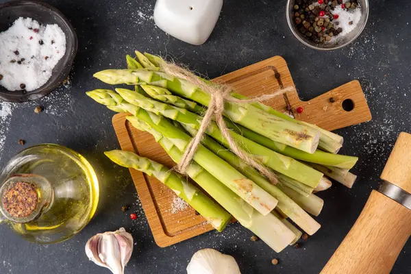 Çiğ organik kuşkonmaz mutfak masasının arka planında bir sürü ev yapımı yeşil kuşkonmaz pişirmeye ve kesme tahtasının üzerinde hazır. Yaz hasadı, yaz yemeği malzemeleri.