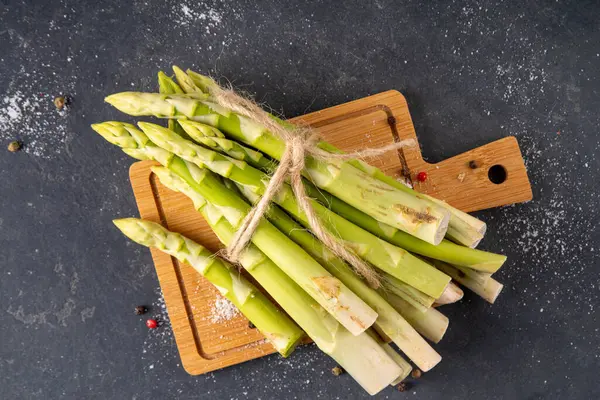 Çiğ organik kuşkonmaz mutfak masasının arka planında bir sürü ev yapımı yeşil kuşkonmaz pişirmeye ve kesme tahtasının üzerinde hazır. Yaz hasadı, yaz yemeği malzemeleri.
