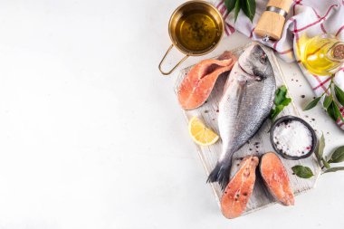 Çiğ balık ve deniz ürünleri pişirme geçmişi, çeşitli taze ve baharatlı dilimlenmiş balıklar, limon, zeytin yağı hazırlık yemeği için, beyaz masa arkaplanı fotokopi alanı