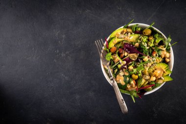 Bitki temelli keto yiyecekler, düşük karbonhidratlı vegan salatası çeşitli yeşil sebzeler, avokado, roka, ıspanak, marul, beyaz peynir, fındık, fıstık, fıstık ezmesi, avokado ve zeytin.