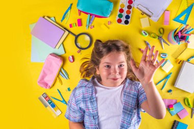 Sevimli duygusal kız okula dönmeye hazır çeşitli okul malzemeleriyle, parlak sarı arka planda eğitim aksesuarlarıyla.