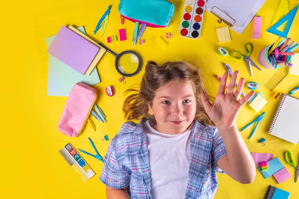 Sevimli duygusal kız okula dönmeye hazır çeşitli okul malzemeleriyle, parlak sarı arka planda eğitim aksesuarlarıyla.