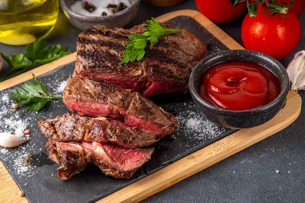 Ahşap kesme tahtasında ızgara biftek, ketçap sosu ve baharat, üst görünüm kopya alanı.