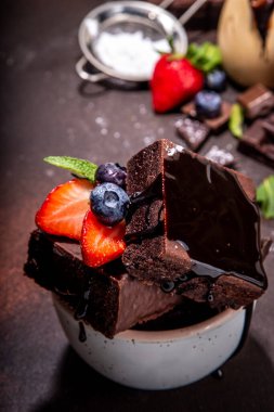 Böğürtlenli siyah çikolatalı kek. Üzerine çikolata sosu serpiştirilmiş ev yapımı kek kurabiyeleri ve koyu arkaplanda taze çilek, yabanmersini, fotokopi alanı.