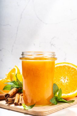 Homemade orange jam in small jar. Homemade orange spicy jam with fresh oranges, cinnamon, mint. Fall preparations and canning on white table background copy space