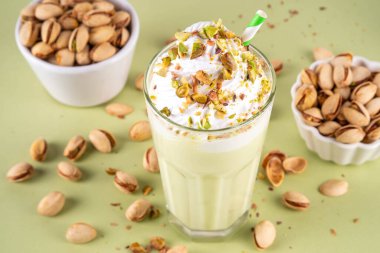 Pistachio milkshake, sağlıklı diyet protein kokteyli, sütsüz kremalı vejetaryen fıstıklı süt, çırpılmış bitkisel krema, fındık serpiştirilmiş, açık yeşil arka plan.