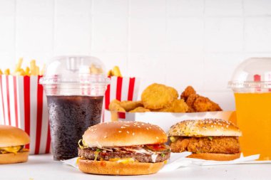 Fast food servis menüsünde çeşitli hamburgerler, cheeseburger, nugget, patates kızartması, gazlı içecek. Ivır zıvır sağlıksız fast food, düşük besinli Ultra işlenmiş gıda, yüksek kalori değeri