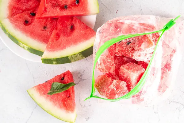 Donmuş karpuz dilimleri, donmuş poşetlerdeki taze çiğ karpuzlar mutfak masasındaki beyaz masa, sağlıklı basit konserve, kış konsepti için dondurulmuş meyve hasadı stokları.. 