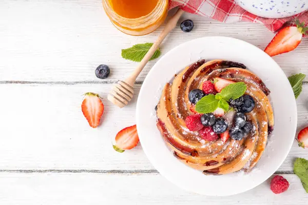 Taze meyve ve böğürtlenli yaz pastası. Geleneksel yuvarlak sünger keki, çilekli mevsimlik tatlı, ahududu, yabanmersini, bal ve şeker serpintileri, beyaz ahşap masa fotokopisi alanı