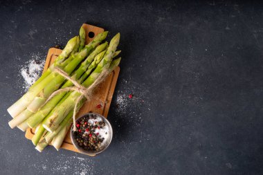 Çiğ organik kuşkonmaz mutfak masasının arka planında bir sürü ev yapımı yeşil kuşkonmaz pişirmeye ve kesme tahtasının üzerinde hazır. Yaz hasadı, yaz yemeği malzemeleri.