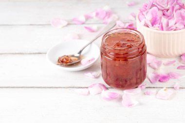 Gül yaprakları reçeli, tatlı çiçek tatlısı, ev yapımı konserve konserveler, organik tatlı gül yaprakları, şeker ve bal, beyaz masada küçük bir kavanozda. Alternatif ilaç, boğaz ağrısı ve soğuk algınlığı için ilaçlar.