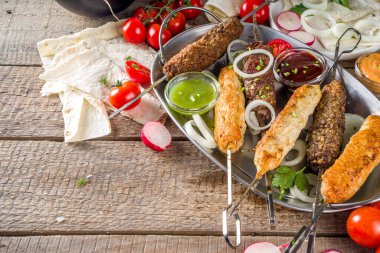 Yaz bbq partisi. Çubukta şiş kebap, kıyma ve tavuk etinden. Lula kebap, geleneksel Kafkas Asya yemeği. Çeşitli soslar, baharatlar ve domateslerle, gri taş arka plan, yukarıdaki boşluğu kopyala