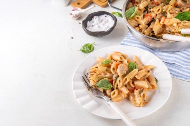 Son moda viral benimle tavuk makarnası evlen. Bir tencere yumuşak makarna ve kremalı ve peynirli sulu tavuk parçaları, sarımsaklı güneşte kurutulmuş domates sosu, nükteli fesleğen yaprağı, tabak ve demlikte.