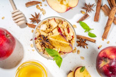 Apple Pie Granola Cheesecake, breakfast snack layered dessert with oat granola, cream cheese yogurt, honey, apple slices and cinnamon spices on white background copy space