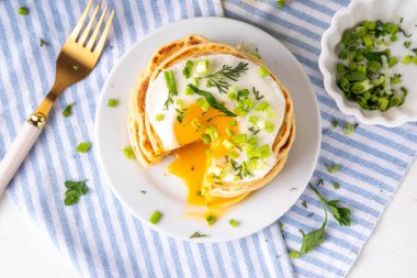 Lezzetli kahvaltı krepleri, taze soğan ve kızarmış yumurta. Lezzetli ya da tatlı olmayan krepleri beyaz mutfak masasında maydanozlu ve güneşli yumurtalarla fotokopi masasının üzerinde.