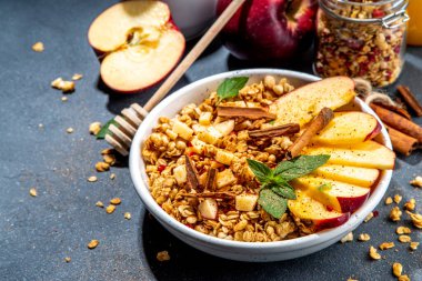 Healthy autumn breakfast granola. Apple pie granola with muesli, cinnamon spices, apples slices, honey and nuts, on black stone background copy space
