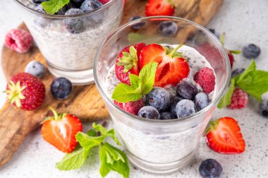 Taze dutlu Chia tohumu pudingi. Sağlıklı yaz kahvaltısı tatlı kremalı süt veya yoğurt, chia, çilek ve yabanmersini, beyaz masa arkaplan fotokopi alanı