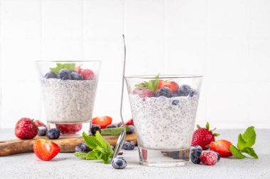 Taze dutlu Chia tohumu pudingi. Sağlıklı yaz kahvaltısı tatlı kremalı süt veya yoğurt, chia, çilek ve yabanmersini, beyaz masa arkaplan fotokopi alanı