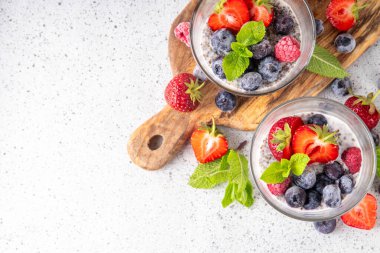 Taze dutlu Chia tohumu pudingi. Sağlıklı yaz kahvaltısı tatlı kremalı süt veya yoğurt, chia, çilek ve yabanmersini, beyaz masa arkaplan fotokopi alanı