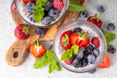 Taze dutlu Chia tohumu pudingi. Sağlıklı yaz kahvaltısı tatlı kremalı süt veya yoğurt, chia, çilek ve yabanmersini, beyaz masa arkaplan fotokopi alanı