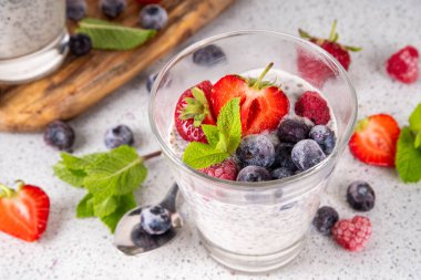 Taze dutlu Chia tohumu pudingi. Sağlıklı yaz kahvaltısı tatlı kremalı süt veya yoğurt, chia, çilek ve yabanmersini, beyaz masa arkaplan fotokopi alanı