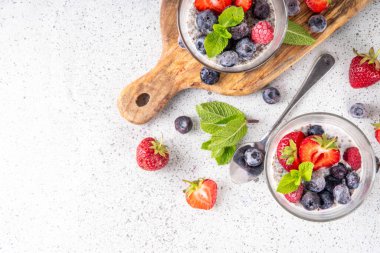Taze dutlu Chia tohumu pudingi. Sağlıklı yaz kahvaltısı tatlı kremalı süt veya yoğurt, chia, çilek ve yabanmersini, beyaz masa arkaplan fotokopi alanı
