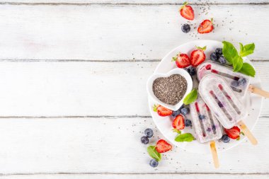 Chia tohumlu dondurma lolipop, ev yapımı sağlıklı detoks dondurma kremalı yoğurt, chia tohumu ve taze yaz meyvesi, beyaz masa fotokopi alanı üzerinde.