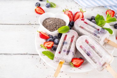 Chia tohumlu dondurma lolipop, ev yapımı sağlıklı detoks dondurma kremalı yoğurt, chia tohumu ve taze yaz meyvesi, beyaz masa fotokopi alanı üzerinde.