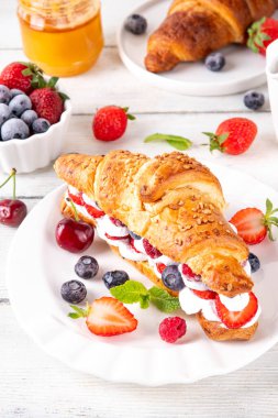 Krem şantili, taze meyve ve meyveli tatlı kahvaltı kruvasan sandviçi. Lezzetli bir yaz yemeği ya da içinde çilek, yabanmersini, kiraz, ahududu ve fındık bulunan taze kruvasanla atıştırmalık bir şeyler.