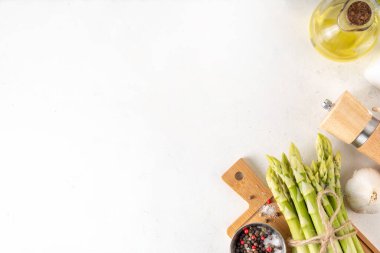 Çiğ organik kuşkonmaz mutfak masasının arka planında bir sürü ev yapımı yeşil kuşkonmaz pişirmeye ve kesme tahtasının üzerinde hazır. Yaz hasadı, yaz yemeği malzemeleri.