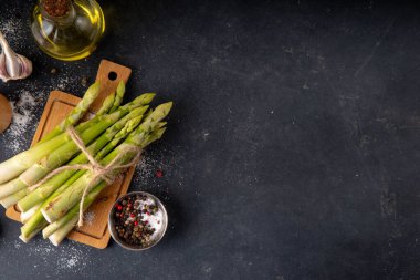 Çiğ organik kuşkonmaz mutfak masasının arka planında bir sürü ev yapımı yeşil kuşkonmaz pişirmeye ve kesme tahtasının üzerinde hazır. Yaz hasadı, yaz yemeği malzemeleri.