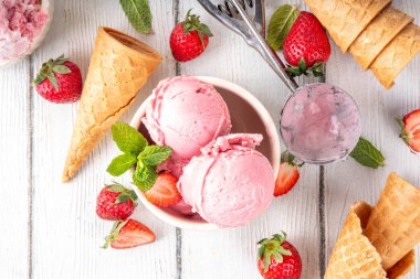 Yaz ferahlatıcı soğuk tatlı, lezzetli ve aromatik çilekli dondurma, seramik kasede ev yapımı meyve şerbeti, taze çilekler, beyaz ahşap arka planda dondurma külahları.