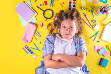 Sevimli duygusal kız okula dönmeye hazır çeşitli okul malzemeleriyle, parlak sarı arka planda eğitim aksesuarlarıyla.
