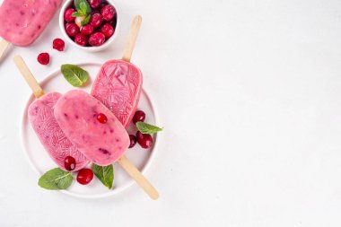 Yabanmersinli dondurma, dondurulmuş kremalı dondurma yoğurt ve böğürtlenli lolipoplar, beyaz tabakta, taze yaban mersinli ve nane yapraklı. 