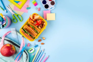 Okula dönelim. Sağlıklı okul yemekleri, çocuklar beslenme çantasına meyve, böğürtlen, fındık ve sebzeli sandviç koydu. Çocukların diyet yemekleri, eğitim okulu malzemeleri, parlak mavi arka plan manzarası.