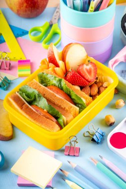 Okula dönelim. Sağlıklı okul yemekleri, çocuklar beslenme çantasına meyve, böğürtlen, fındık ve sebzeli sandviç koydu. Çocukların diyet yemekleri, eğitim okulu malzemeleri, parlak mavi arka plan manzarası.