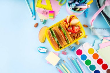 Okula dönelim. Sağlıklı okul yemekleri, çocuklar beslenme çantasına meyve, böğürtlen, fındık ve sebzeli sandviç koydu. Çocukların diyet yemekleri, eğitim okulu malzemeleri, parlak mavi arka plan manzarası.