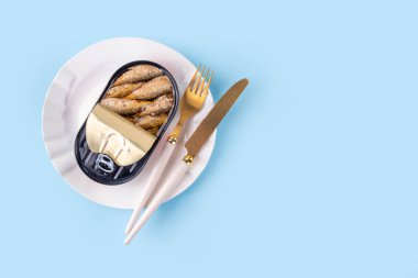 Sardunya trend konsepti, metal konserve sardalyalar mavi arka planda, çatal ve bıçakla tabakta.