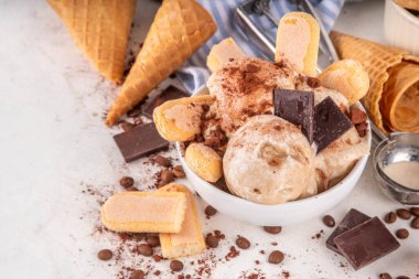 Lezzetli tiramisu dondurması, kahve şurubu, savoyardi kurabiyeleri, çikolata, kakao tozu. Bir kase İtalyan tiramisu tatlı dondurması, dondurmalı waffle konileri, kahve çekirdekleri, malzemeler.