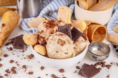 Lezzetli tiramisu dondurması, kahve şurubu, savoyardi kurabiyeleri, çikolata, kakao tozu. Bir kase İtalyan tiramisu tatlı dondurması, dondurmalı waffle konileri, kahve çekirdekleri, malzemeler.
