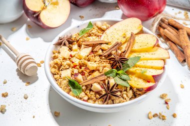 Healthy autumn breakfast granola. Apple pie granola with muesli, cinnamon spices, apples slices, honey and nuts, on white stone background copy space