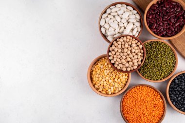 Çeşitli kuru fasulyeler, mercimek, mung, nohut, ahşap kaselerde bezelye çeşitleri. Legumes beyaz masa üst görünümünde. Vegan protein kaynakları yiyecek, kopyalama alanı