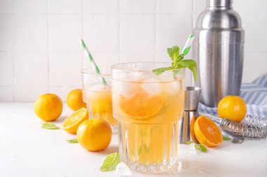 Mandalina tatlısı ve ekşi limonata, portakal suyu, taze mandalina ve nane yapraklı buzlu narenciye alkollü kokteyli, beyaz masa arkasında fotokopi alanı.