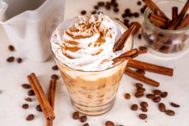 Krem şantili buzlu tarçınlı latte, tarçın şurubu ve tarçın tozu, beyaz ve bej arkaplan fotokopi alanı üzerine kahve çekirdekleri.