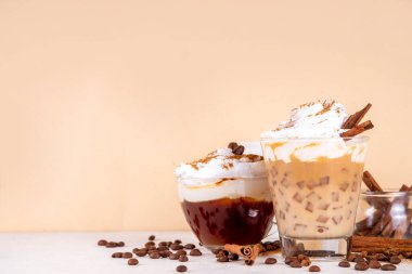 Krem şantili buzlu tarçınlı latte, tarçın şurubu ve tarçın tozu, beyaz ve bej arkaplan fotokopi alanı üzerine kahve çekirdekleri.