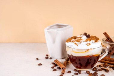 Krem şantili buzlu tarçınlı latte, tarçın şurubu ve tarçın tozu, beyaz ve bej arkaplan fotokopi alanı üzerine kahve çekirdekleri.