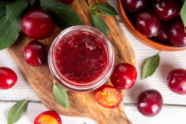 Küçük kavanozda kiraz eriği reçeli. Ev yapımı sonbahar kırmızı kirazlı erik reçeli ve taze meyveli reçel. Sonbahar hazırlıkları, meyve reçelleri tahta masa arkaplan kopyalama alanı üzerinde konserveler