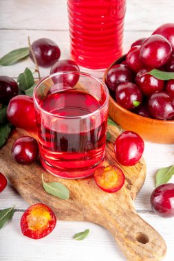 Tatlı ve lezzetli kırmızı kiraz suyu, sürahi ve bardakta, taze kiraz eriği meyveleri ve ağaç yaprakları beyaz arka planda, kopyalama alanı
