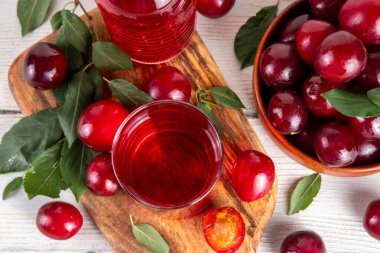 Tatlı ve lezzetli kırmızı kiraz suyu, sürahi ve bardakta, taze kiraz eriği meyveleri ve ağaç yaprakları beyaz arka planda, kopyalama alanı